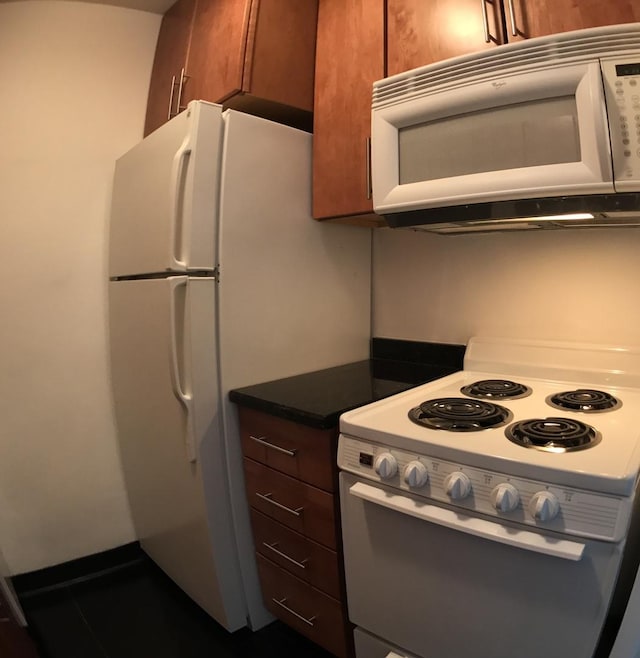 kitchen featuring white appliances, dark countertops, and brown cabinets
