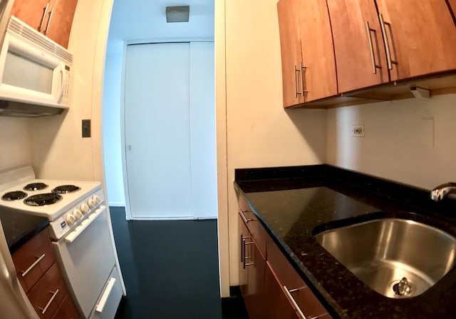 kitchen featuring white appliances, a sink, dark stone countertops, and brown cabinetry