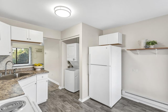 kitchen with freestanding refrigerator, stacked washing machine and dryer, baseboard heating, a sink, and dark wood-style flooring