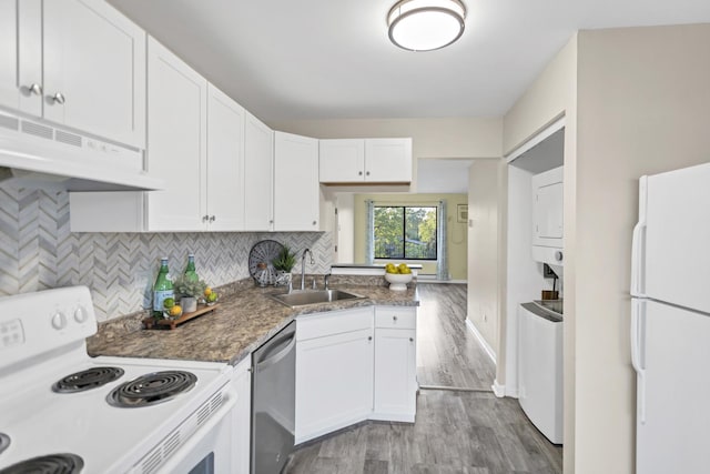 kitchen with white appliances, a sink, stacked washing machine and dryer, under cabinet range hood, and white cabinetry