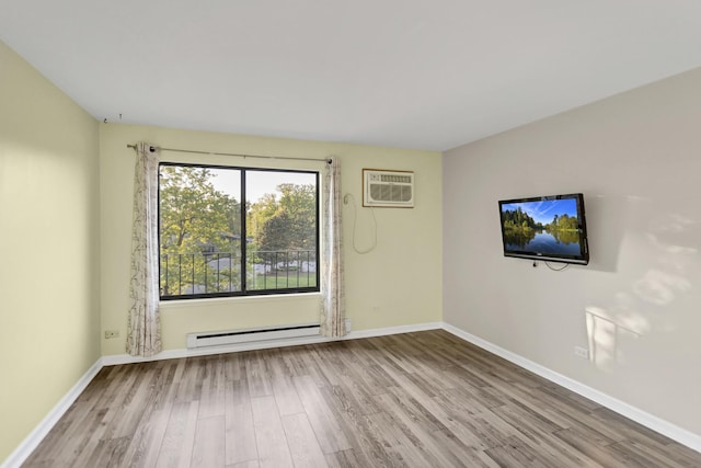 unfurnished room with a baseboard heating unit, a wall mounted air conditioner, wood finished floors, and baseboards