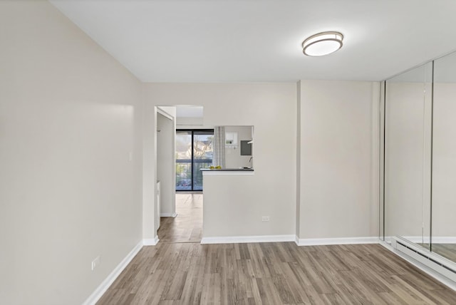 unfurnished room featuring wood finished floors, baseboards, and a baseboard heating unit
