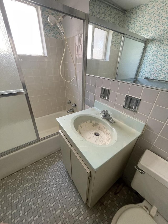 full bathroom featuring toilet, wallpapered walls, tile walls, shower / bath combination with glass door, and vanity