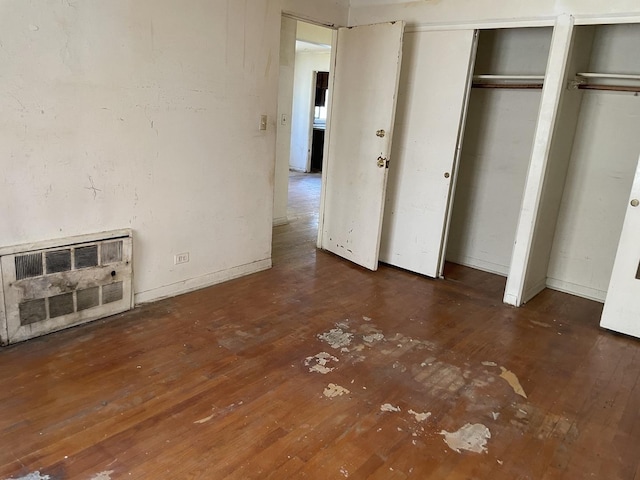 unfurnished bedroom with heating unit, hardwood / wood-style flooring, multiple closets, and baseboards
