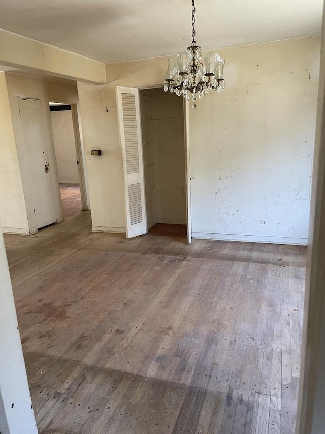 unfurnished dining area featuring wood-type flooring, a chandelier, and baseboards