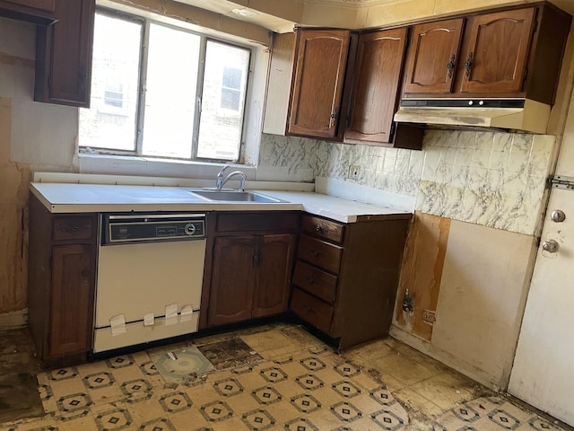 kitchen featuring white dishwasher, a sink, under cabinet range hood, light countertops, and backsplash