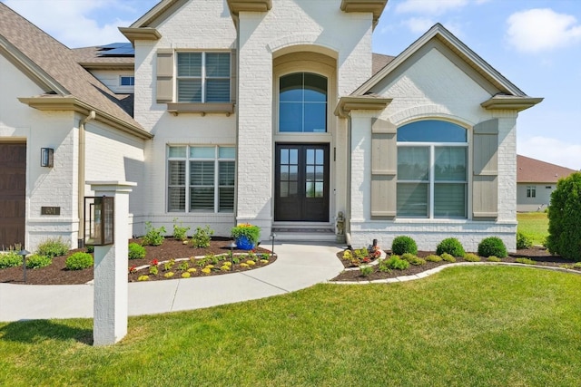 604 Cayman Way, Savoy, IL 61874 - view of front facade with french doors, a front lawn, brick siding, and a shingled roof