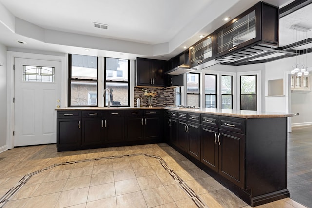 kitchen featuring dark cabinetry, baseboards, a sink, wall chimney exhaust hood, and recessed lighting