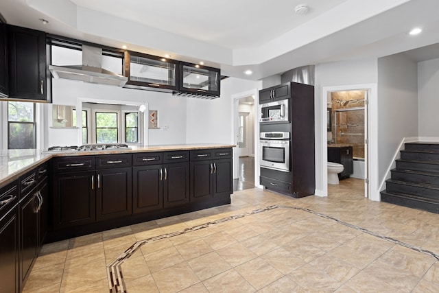 kitchen with stainless steel appliances, recessed lighting, dark cabinetry, light stone counters, and inlaid floor details