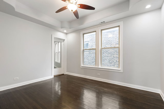 empty room with baseboards, dark wood finished floors, a ceiling fan, a raised ceiling, and recessed lighting
