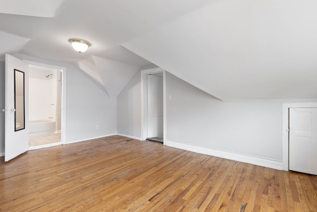 additional living space with light wood-type flooring, vaulted ceiling, and baseboards