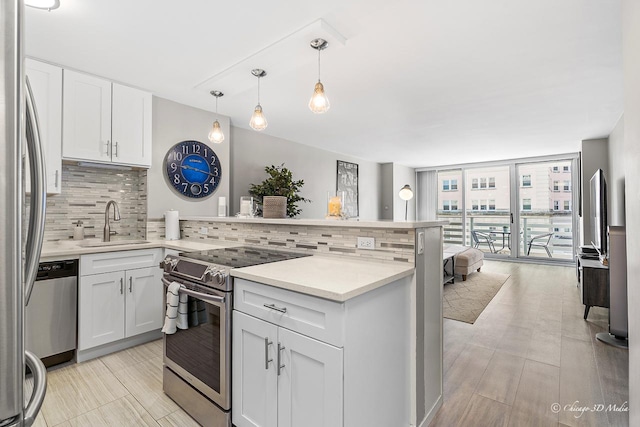 kitchen featuring appliances with stainless steel finishes, a sink, expansive windows, backsplash, and a peninsula