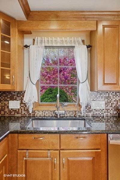 kitchen featuring a sink, stainless steel dishwasher, glass insert cabinets, and dark stone counters
