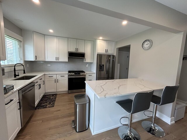 617 S Albert St, Mount Prospect, IL 60056 - kitchen featuring stainless steel appliances, a sink, light wood-type flooring, light stone counters, and a breakfast bar