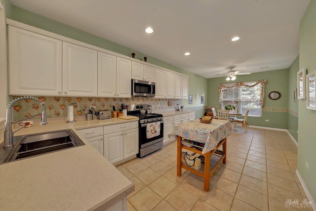 kitchen with stainless steel appliances, a sink, a ceiling fan, backsplash, and light countertops