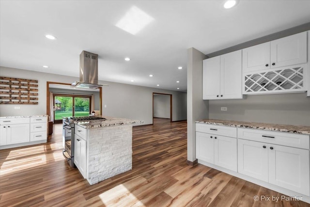 kitchen featuring island range hood, stainless steel range with gas stovetop, white cabinetry, wood finished floors, and recessed lighting