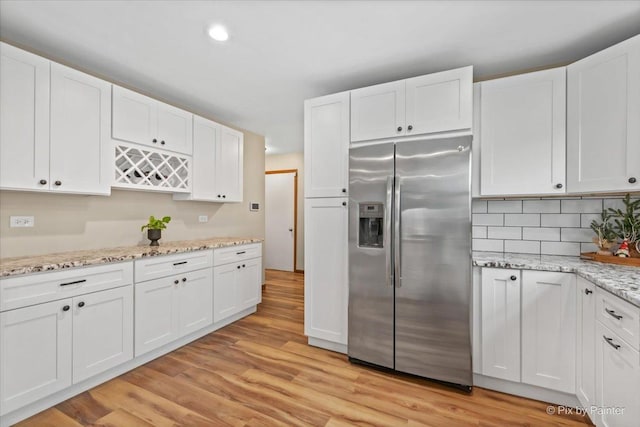 kitchen with stainless steel fridge, white cabinetry, light wood-type flooring, tasteful backsplash, and light stone counters