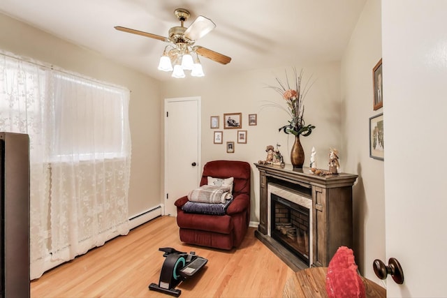 sitting room with a ceiling fan, wood finished floors, baseboard heating, and a fireplace