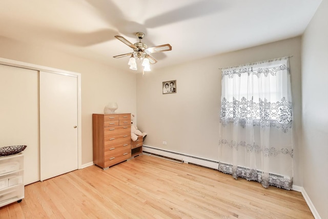 bedroom featuring a baseboard heating unit, light wood-style flooring, a closet, a ceiling fan, and baseboards