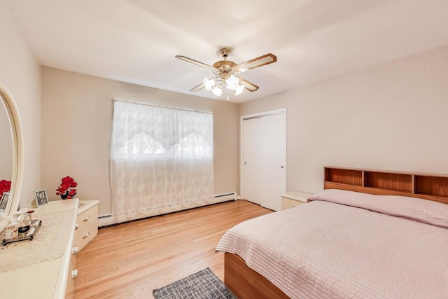 bedroom featuring baseboard heating, light wood-style flooring, ceiling fan, and a closet