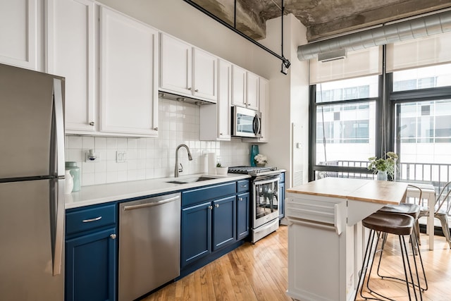 210 S Desplaines St Unit 402, Chicago, IL 60661 - kitchen featuring stainless steel appliances, blue cabinets, a sink, light wood finished floors, and tasteful backsplash