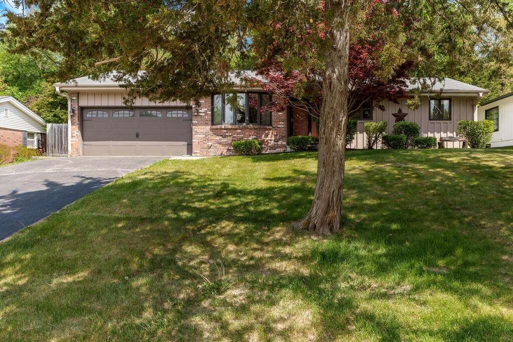 4922 Brookview Rd, Rockford, IL 61107 - view of property hidden behind natural elements featuring asphalt driveway, board and batten siding, a garage, a front lawn, and brick siding