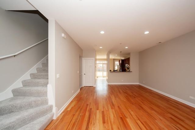 unfurnished living room featuring stairway, light wood-style flooring, baseboards, and recessed lighting