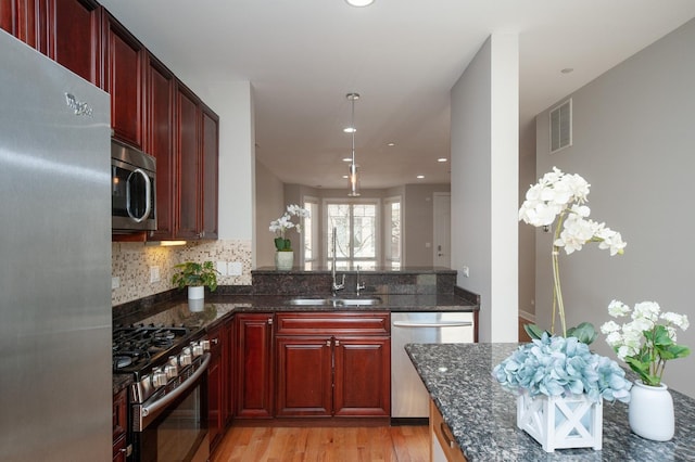kitchen featuring stainless steel appliances, reddish brown cabinets, a sink, dark stone countertops, and recessed lighting
