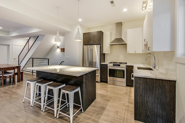 1300 N Artesian Ave Unit F, Chicago, IL 60622 - kitchen with appliances with stainless steel finishes, wall chimney range hood, a sink, a breakfast bar, and light wood-style flooring