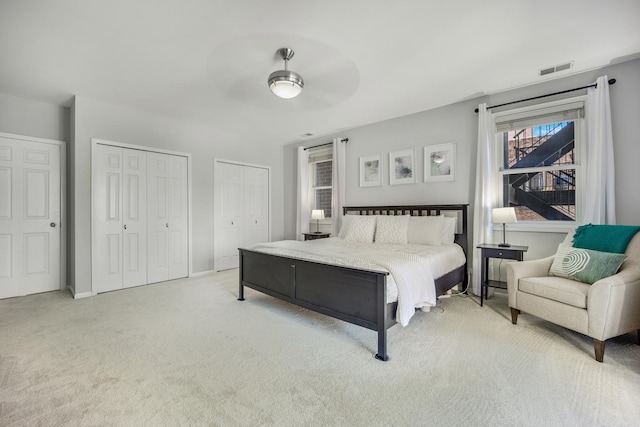 bedroom featuring multiple closets, light colored carpet, and ceiling fan