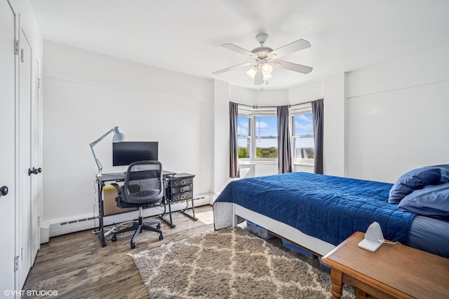 bedroom with a baseboard radiator, wood finished floors, ceiling fan, and an office area