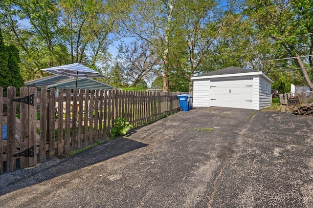 view of yard with an outdoor structure, a garage, fence, and asphalt driveway