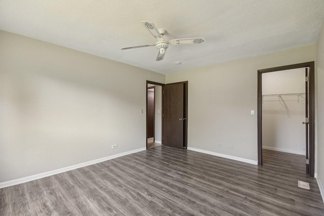 unfurnished bedroom featuring dark wood-style floors, a closet, a textured ceiling, a spacious closet, and baseboards