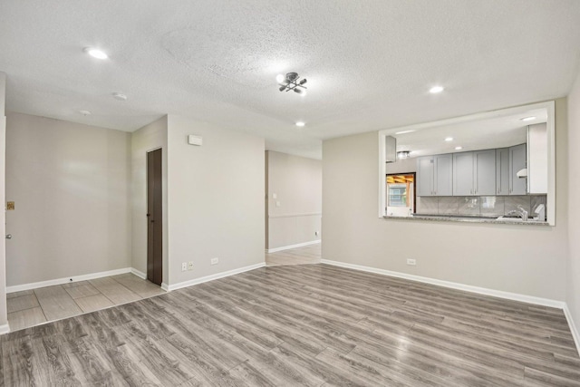 unfurnished living room featuring wood finished floors, recessed lighting, a textured ceiling, and baseboards