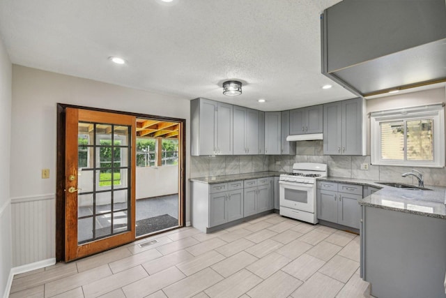 kitchen featuring white range with gas cooktop, gray cabinets, a sink, light stone countertops, and tasteful backsplash