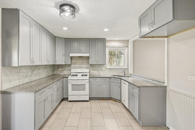 kitchen with white appliances, a sink, gray cabinetry, light stone counters, and tasteful backsplash