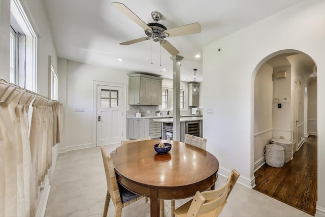 dining area featuring a ceiling fan, arched walkways, beverage cooler, baseboards, and recessed lighting