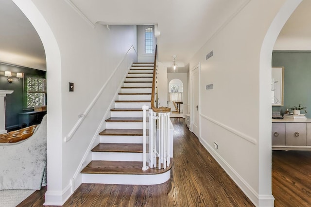 stairway with wood finished floors, plenty of natural light, and arched walkways