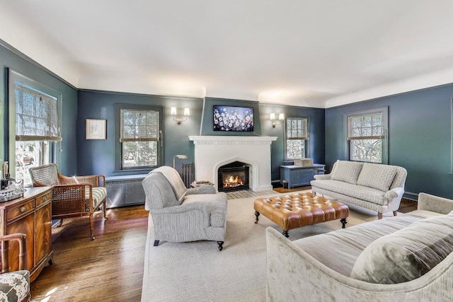 living room with a fireplace with flush hearth, wood finished floors, and crown molding