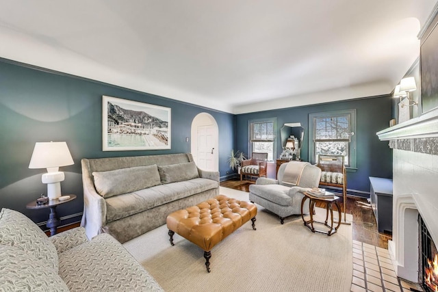 tiled living room featuring a fireplace with flush hearth, baseboards, arched walkways, and a baseboard heating unit