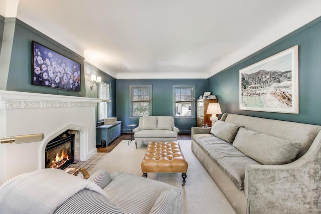 living room with a lit fireplace, wood finished floors, baseboards, and ornamental molding