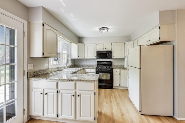 kitchen featuring black appliances, a peninsula, light wood-style floors, a sink, and white cabinetry