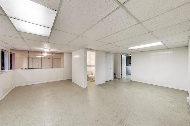 finished below grade area featuring a paneled ceiling, stairway, and baseboards