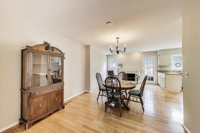 dining area featuring a chandelier, light wood-style flooring, a fireplace, and baseboards