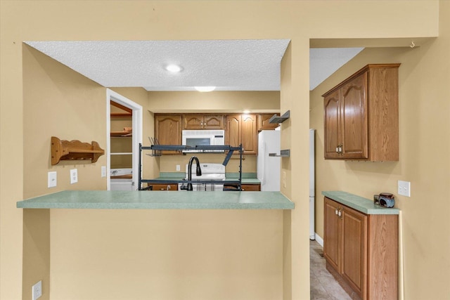 1109 Pomona Dr Unit 1109, Champaign, IL 61822 - kitchen with white appliances, a peninsula, brown cabinetry, a textured ceiling, and light countertops