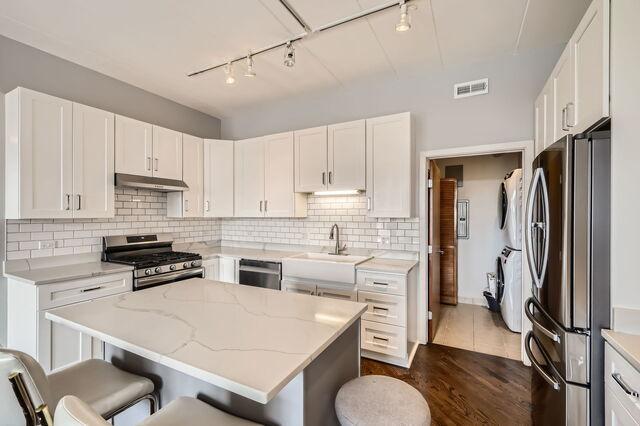1405 N Orleans St Unit 5N, Chicago, IL 60610 - kitchen featuring stainless steel appliances, stacked washing machine and dryer, under cabinet range hood, rail lighting, and light stone counters