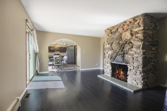 unfurnished living room with a baseboard heating unit, arched walkways, wood finished floors, and baseboards