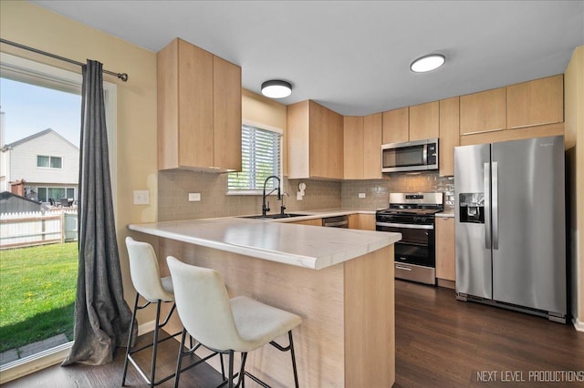 kitchen with appliances with stainless steel finishes, light brown cabinetry, a sink, and a peninsula