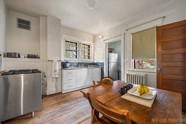 kitchen featuring radiator heating unit, freestanding refrigerator, white cabinetry, light wood finished floors, and a sink