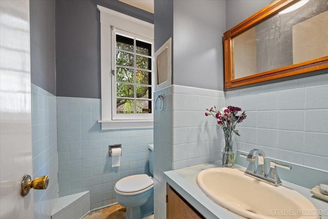 half bathroom with tile walls, toilet, vanity, and a wainscoted wall